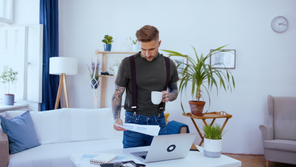 Young man with laptop standing indoors at desk in home office, working.