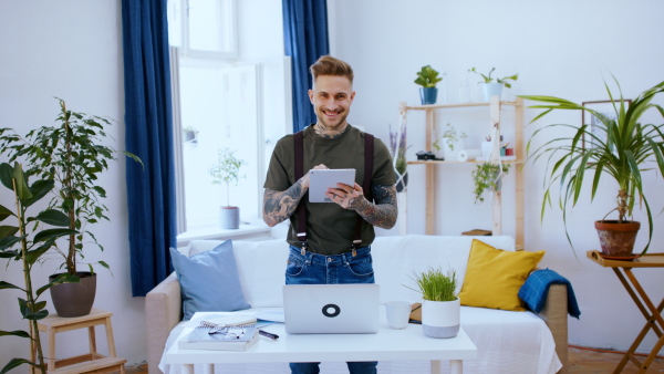 Front view portrait of man with tablet standing indoors at desk in home office, using tablet.