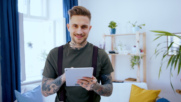 Front view portrait of man with tablet standing indoors at desk in home office, using tablet.