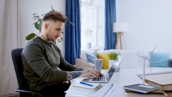 Young man with laptop sitting indoors at desk in home office, working.