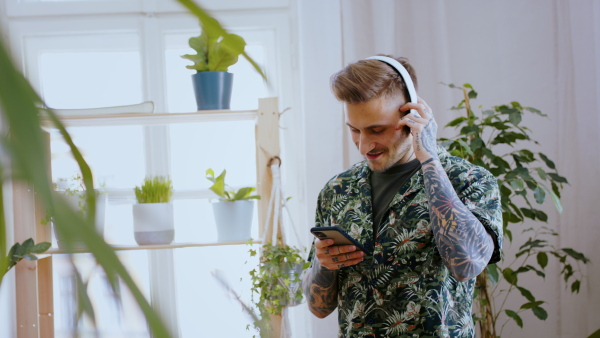 Portrait of man with smartphone and headphones indoors at home, listening to music.