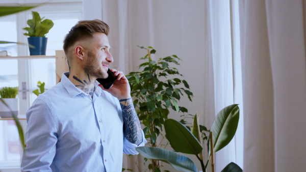 Young man with smartphone standing indoors in home office, making phone call.