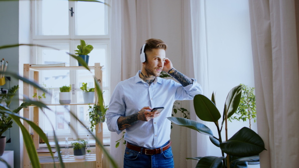 Portrait of man with smartphone and headphones indoors at home, listening to music.