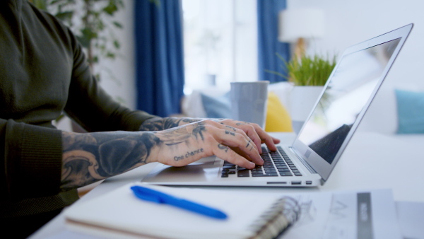 Unrecognizable young man with laptop sitting indoors at desk in home office, working.