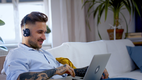 Side view of man with laptop working indoors on sofa in home office, video call concept.