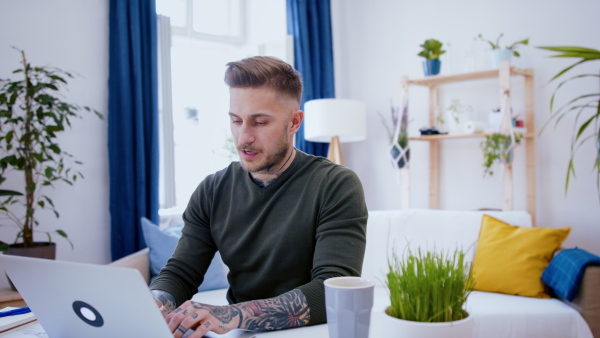 Young man with laptop working indoors at desk in home office, video call concept.