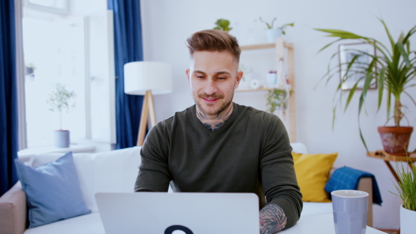 Front view of man with laptop working indoors at desk in home office, video call concept.