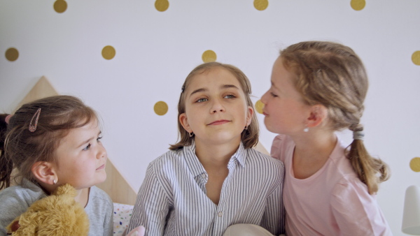 A front view of three girls sisters indoors at home, kissing.