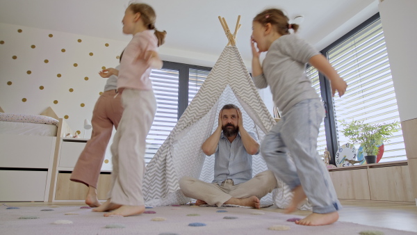 A frustrated father with daughters indoors at home, playing and having fun.