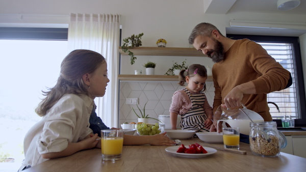 A father with three daughters indoors at home, eating breakfast in kitchen.