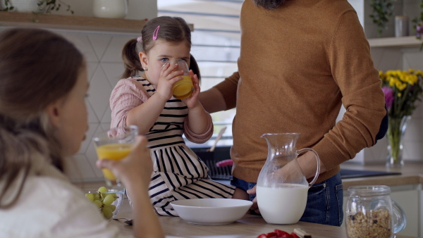 An unrecognizable father with two daughters indoors at home, eating breakfast in kitchen.