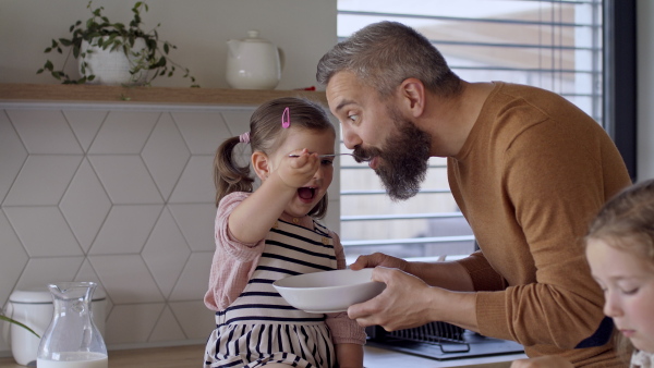 A father with three daughters indoors at home, eating breakfast in kitchen.