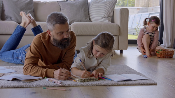 Mature father with daughters indoors at home, drawing pictures on floor.