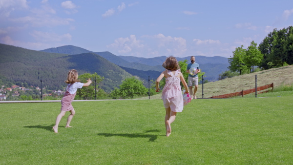 A father with daughters playing outdoors in the backyard, running.