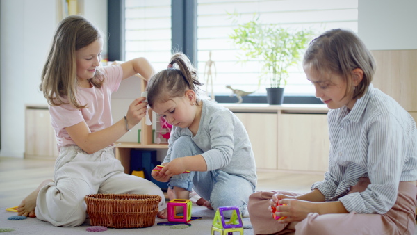 A front view of three sisters indoors at home, playing on floor.