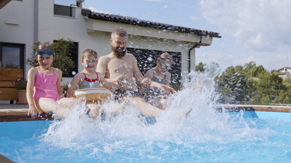 A father with three daughters outdoors in the backyard, sitting by swimming pool.