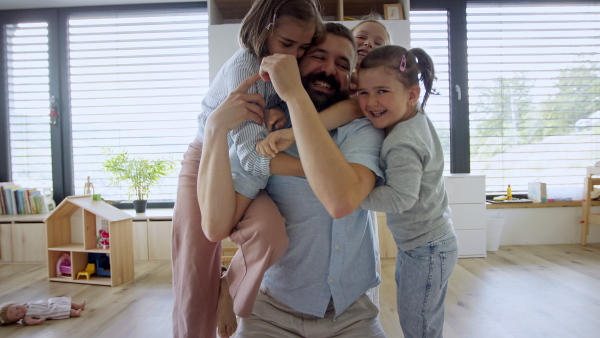 A father with three daughters indoors at home, playing on floor and looking at camera.