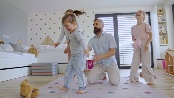 A father with three daughters indoors at home, playing on floor and jumping.