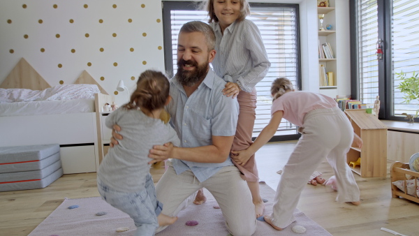 A father with three daughters indoors at home, playing on floor and jumping.