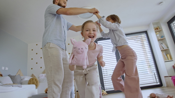 A low angle view of father with three daughters indoors at home, playing on floor and dancing.