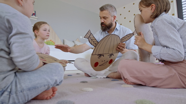 A father with three daughters indoors at home, playing on floor.