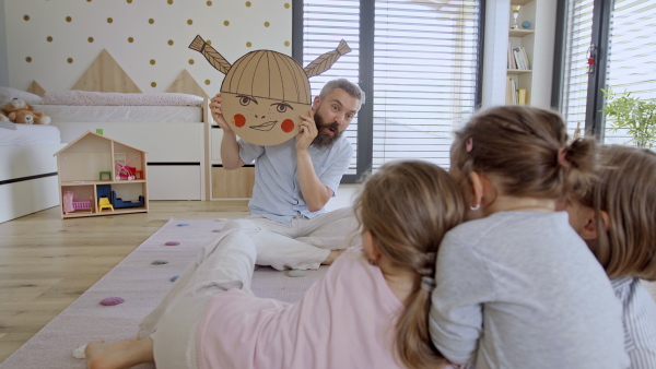 A father with three daughters indoors at home, playing on floor.