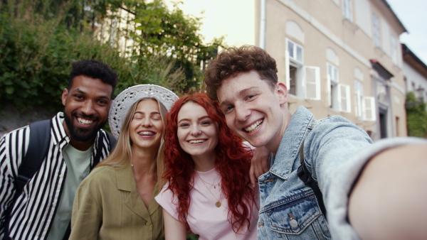 A group of young people outdoors on trip in town, taking selfie and looking at camera.