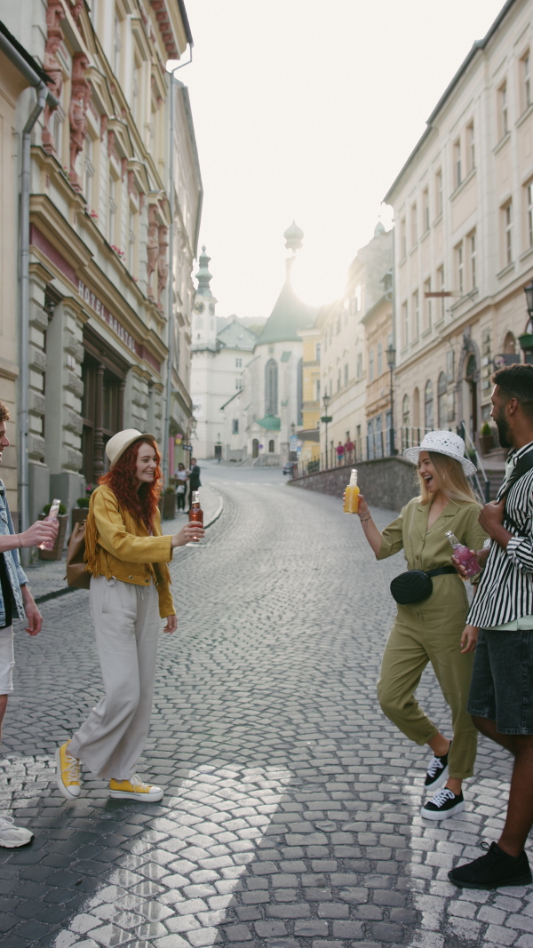 A vertical footage of happy young people with drinks outdoors on street on town trip, laughing.