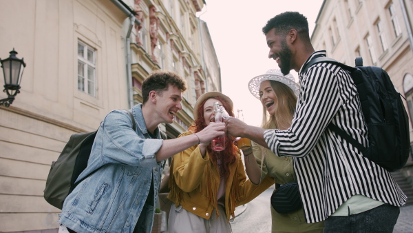 A group of happy young people with drinks outdoors on street on town trip, laughing.