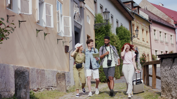 A front view of group of happy young people outdoors on trip in town, walking and talking.