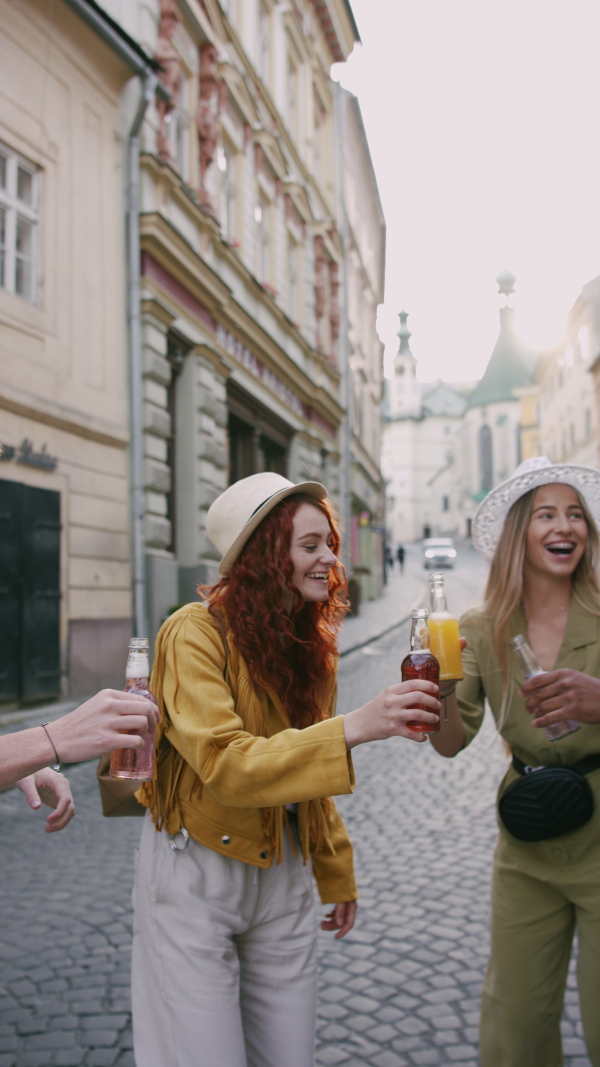 A vertical footage of happy young people with drinks outdoors on street on town trip, laughing.