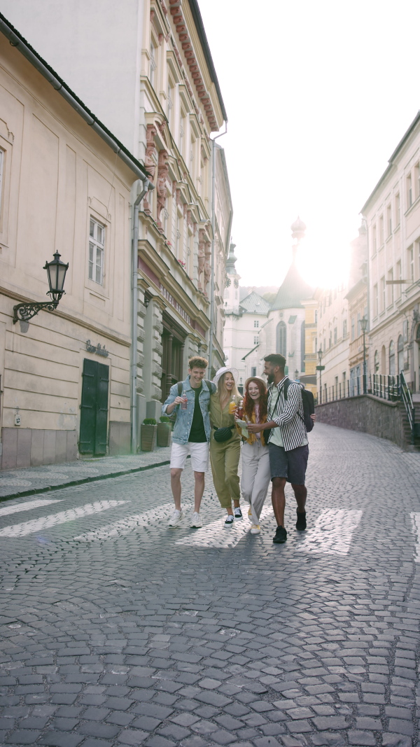 A vertical footage of group of happy young people outdoors on street on town trip, walking with drinks.