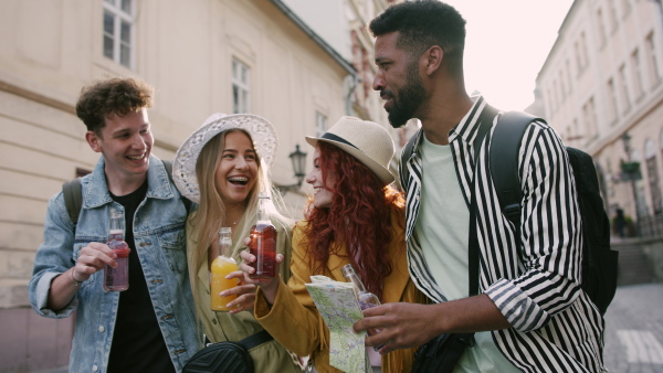 A front view of group of happy young people outdoors on street on town trip, walking with drinks.