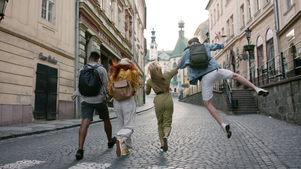 A rear view of group of young people outdoors on trip in town, running, jumping and holding hands.