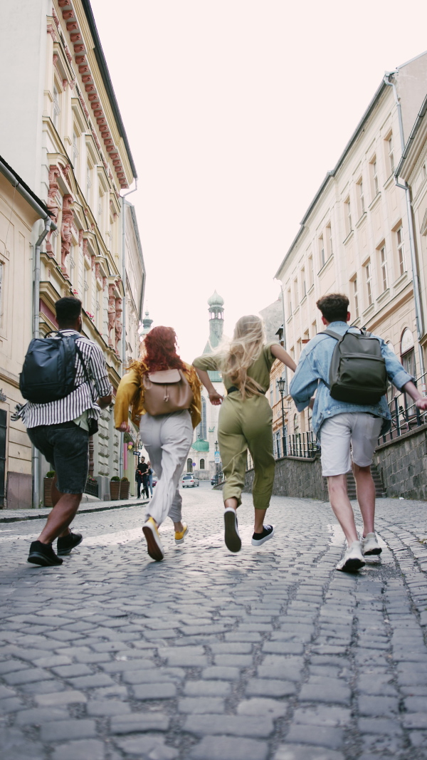 A vertical footage of group of young people outdoors on trip in town, running, jumping and holding hands.