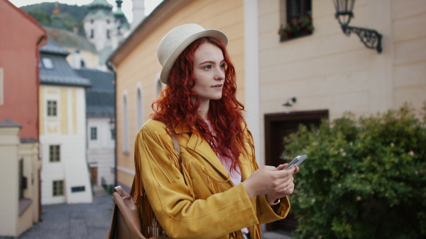 A young woman outdoors on trip in town, using online map on smartphone and looking at camera.