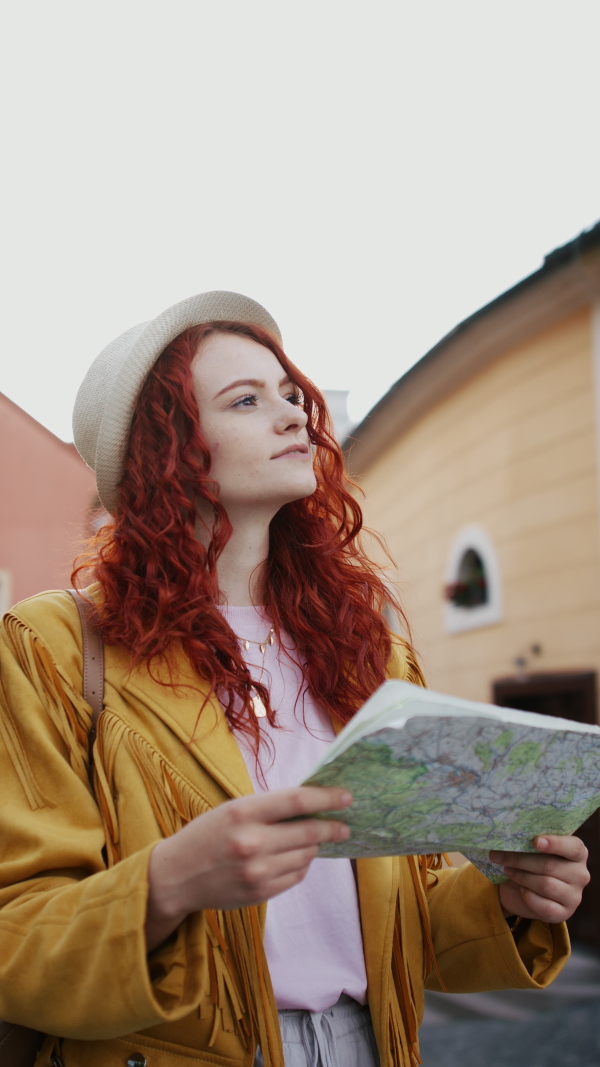 A vertical footage of young woman tourist outdoors on trip in town, using map.