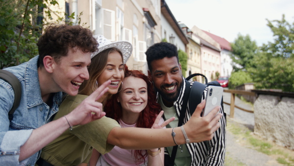 A group of young people outdoors on trip in town, taking selfie.