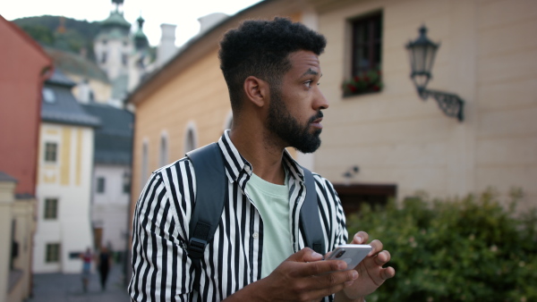 A young man outdoors on trip in town, using online map on smartphone.