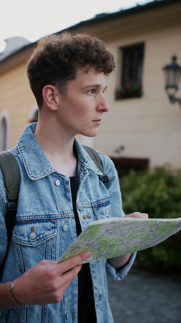 A vertical footage of young man tourist outdoors on trip in town, using map.