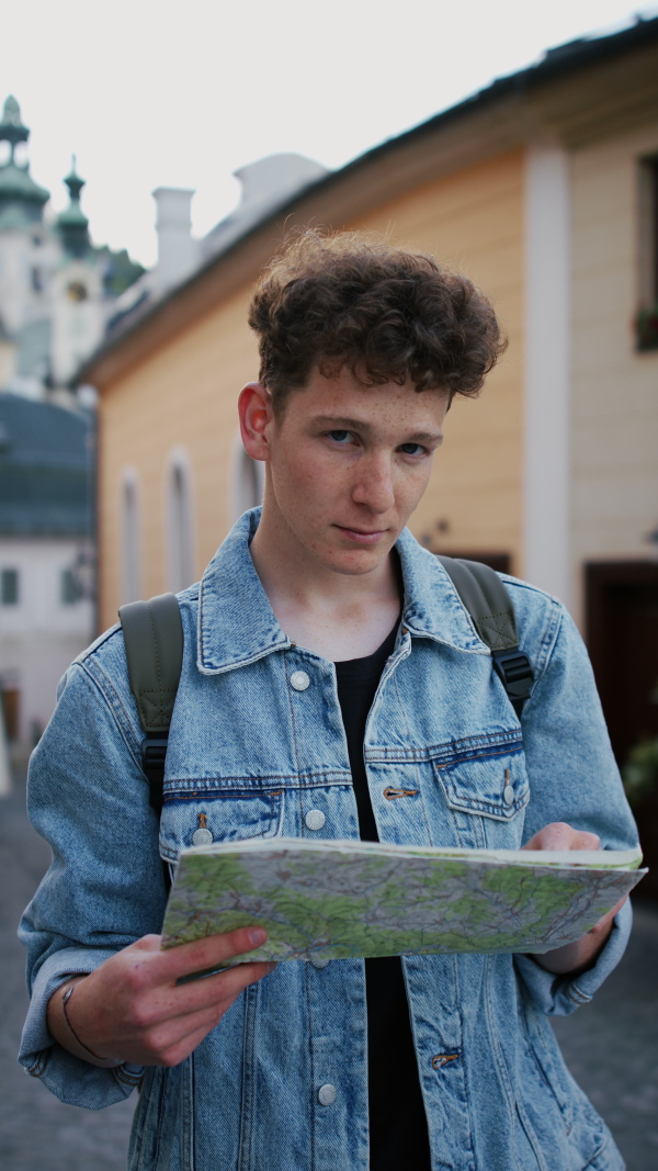 A vertical footage of young man tourist outdoors on trip in town, using map and looking at camera.