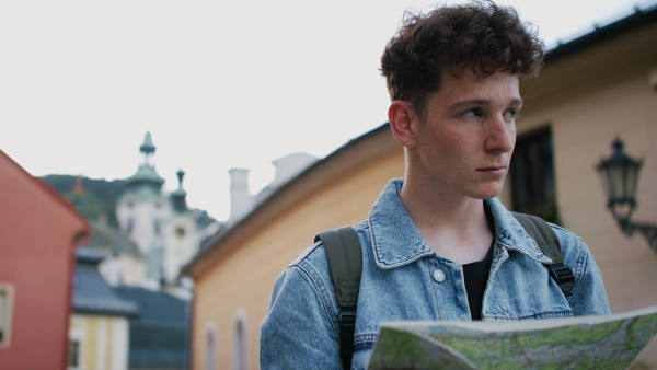 A young man tourist outdoors on trip in town, using map.