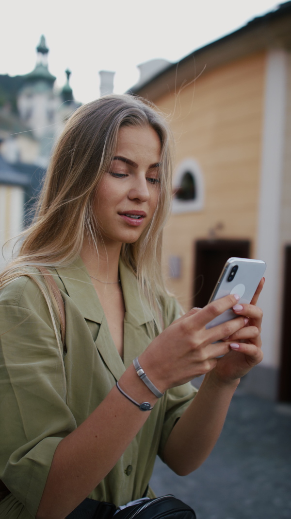 Vertical footage of happy young woman tourist outdoors on trip in town, using online map on smartphone.