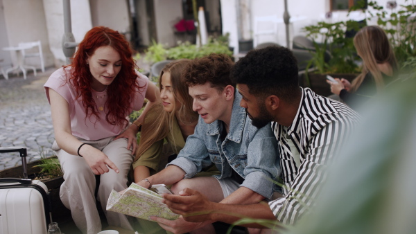 A group of happy young people sitting in outdoors cafe on town trip, using map.