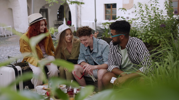 A group of happy young people sitting in outdoors cafe on town trip, looking at camera and taking selfies.