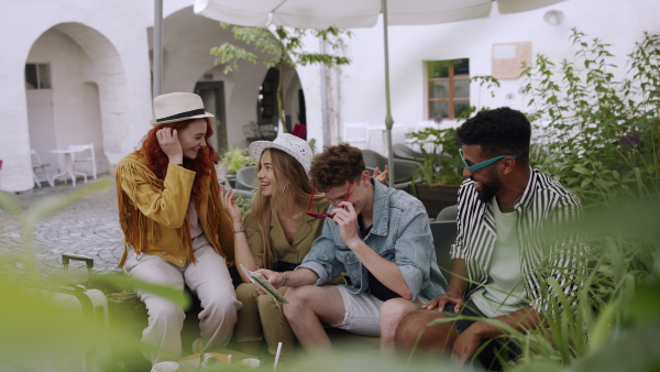 A group of happy young people sitting in outdoors cafe on town trip, using map.