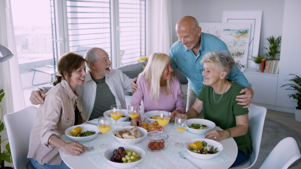 A group of senior friends having party indoors, eating at the table and looking at camera.