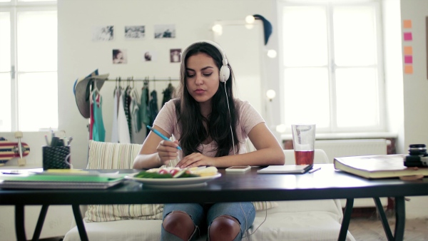 A young teenage girl with headphones sitting indoors, listening to music.