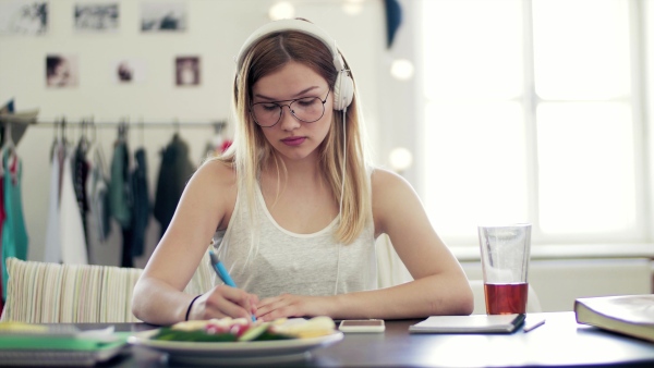 A young teenage girl with headphones sitting indoors, listening to music.