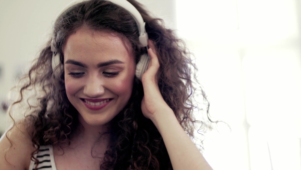 A close-up of young teenage girl with headphones sitting indoors, listening to music.